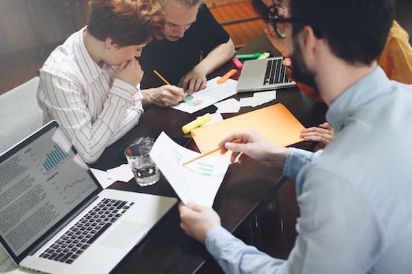 Anklyticx - A group of people sitting around a table with papers and laptops.